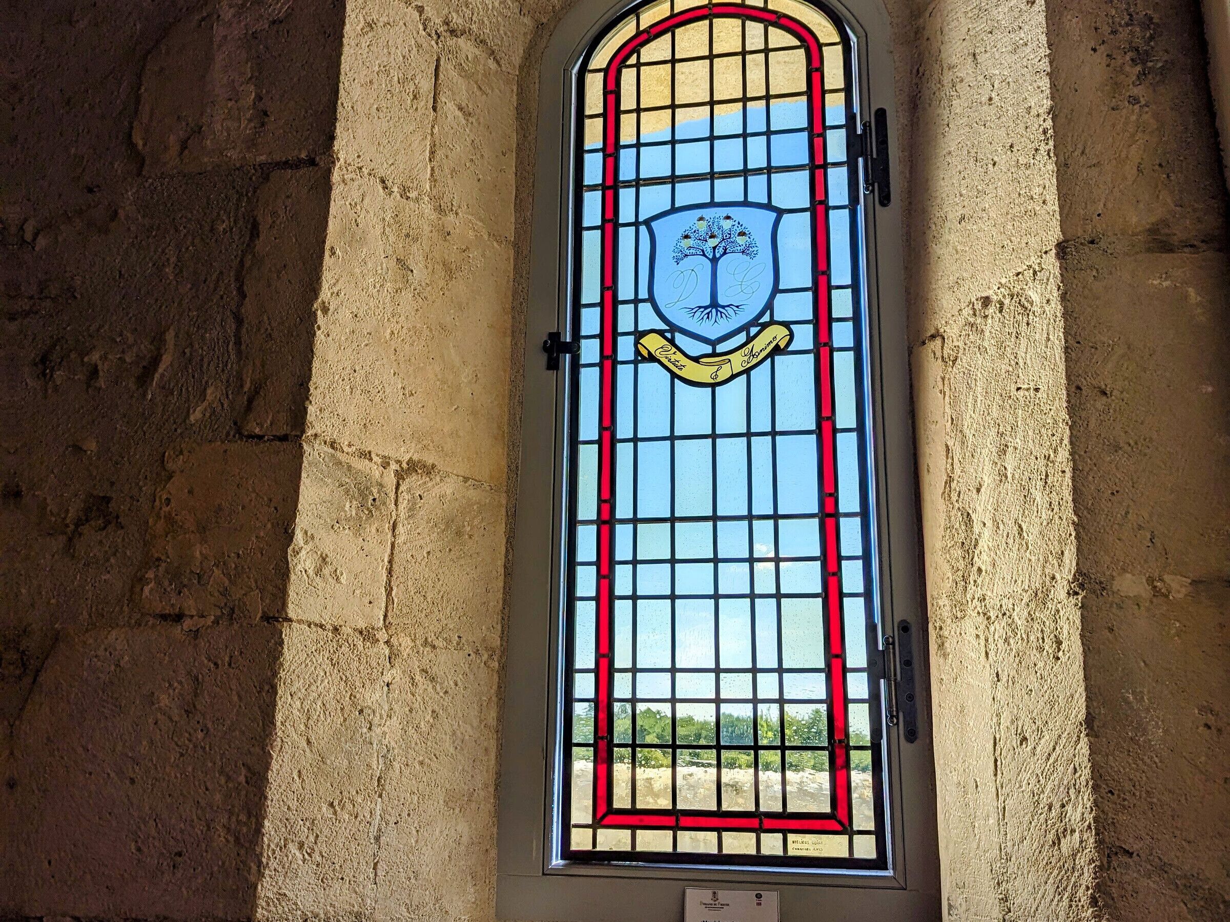 A stained glass window with a tree emblem, a shield, and a banner.