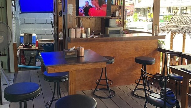 Una cafetería con mostrador de madera, taburetes de bar y una pantalla de televisión mostrando un programa.