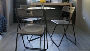Cocina compacta con microondas, pileta y ventana. Hay dos sillas plegables y una mesita.