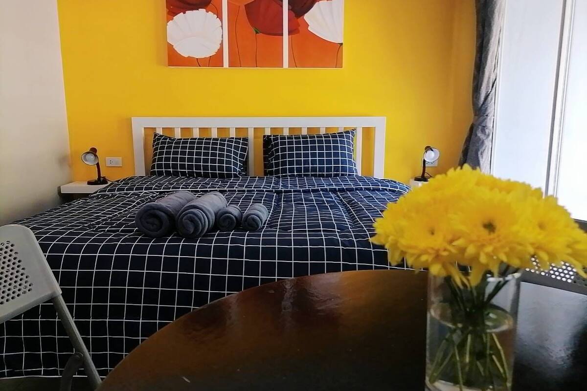 A hotel room with a bed, a nightstand, a desk, a chair, and a vase with flowers.