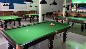 Una sala de billar con varias mesas e iluminación colgante.