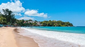 Una playa con aguas azules cristalinas, una orilla arenosa y edificios al fondo.