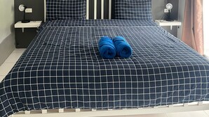 Un dormitorio con cama, dos mesitas de noche, un cuadro colgado en la pared y una ventana con cortinas.