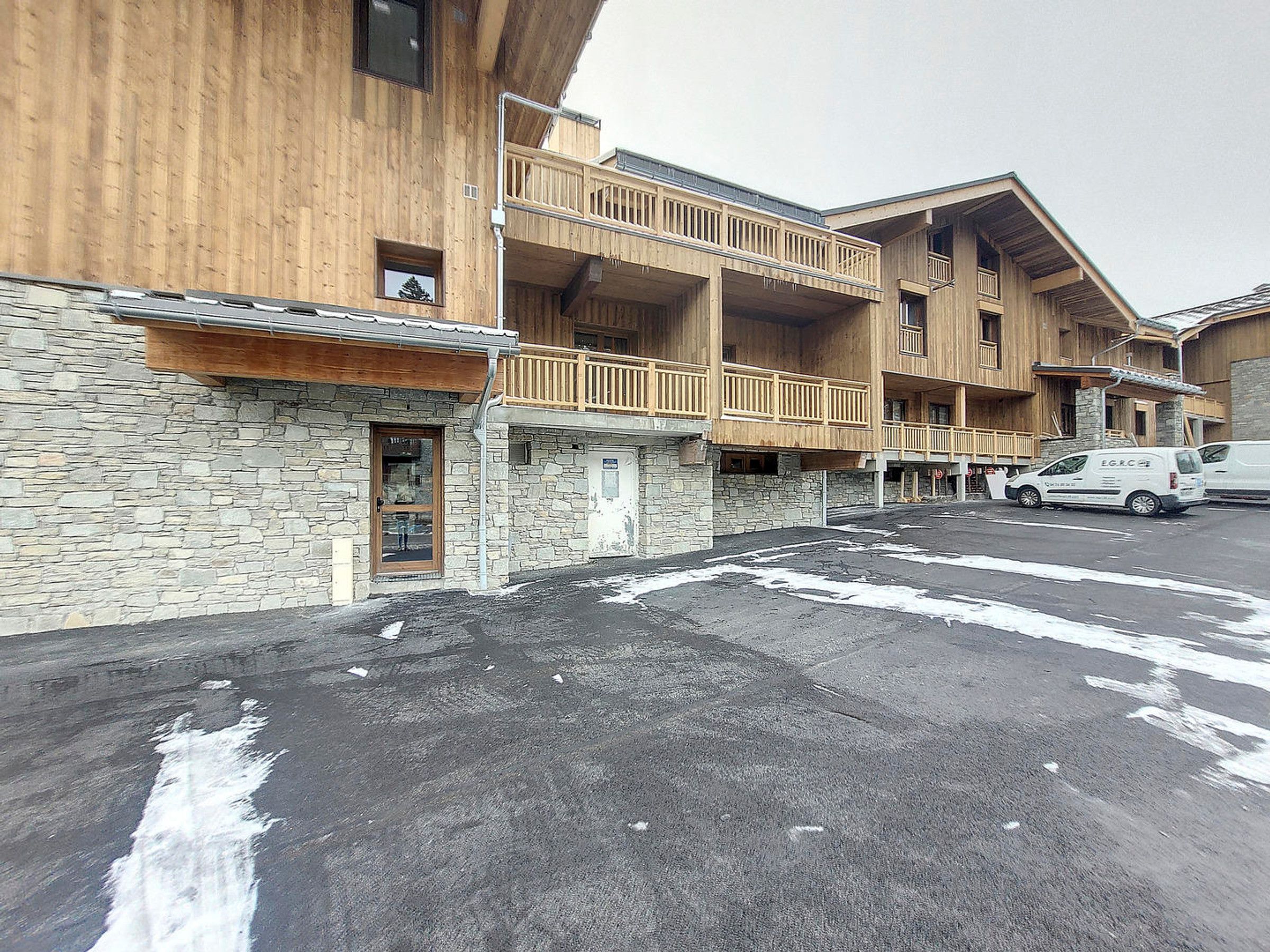 A multi-story wooden building with balconies, a stone facade, and a parking area with a van.