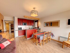 A compact kitchen with red cabinets, a dining area with a table and chairs, and a wooden floor. - Bright 3-room apartment - La Rosière - Balcony, Parking - 6 pers (Montvalezan-La Rosière)