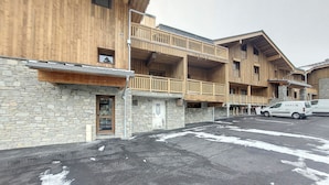 A multi-story wooden building with balconies, a stone facade, and a parking area with a van. - Bright 3-room apartment - La Rosière - Balcony, Parking - 6 pers (Montvalezan-La Rosière)