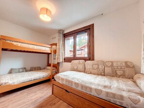 Una habitación con literas, una ventana con cortinas y suelo de madera.