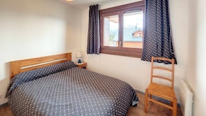 A bedroom with a bed, a chair, a nightstand, a lamp, and a window with curtains. - Bright 3-room apartment - La Rosière - Balcony, Parking - 6 pers (Montvalezan-La Rosière)