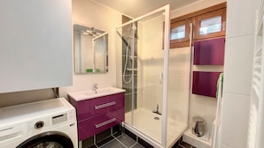 A compact bathroom with a washing machine, a glass-enclosed shower, and a vanity with purple cabinets. - Bright 3-room apartment - La Rosière - Balcony, Parking - 6 pers (Montvalezan-La Rosière)