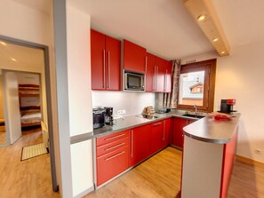 Una cocina compacta con armarios rojos, un microondas, una cafetera y un lavamanos.