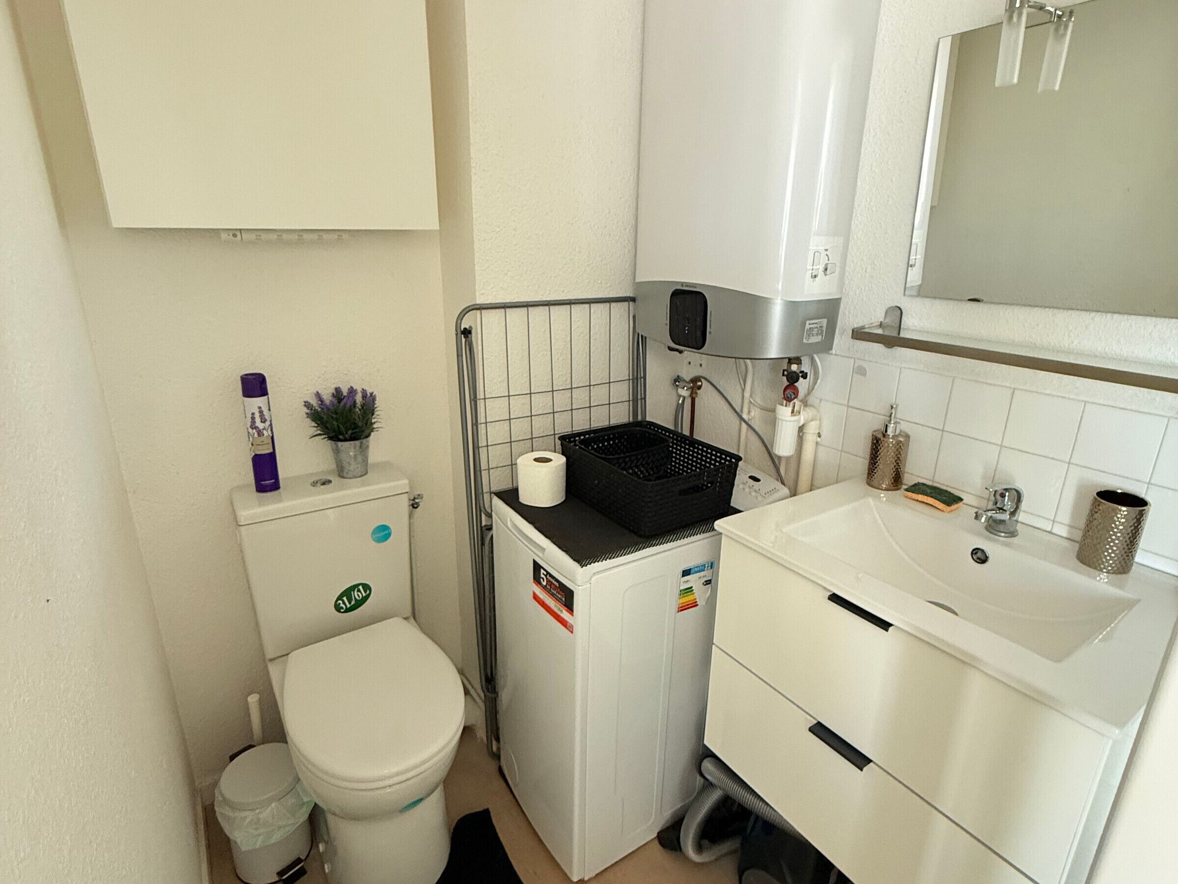 Ein kleines Badezimmer mit Toilette, Waschmaschine, Waschbecken und Spiegel.