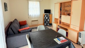 Un espacio habitable compacto con sofá, una mesa de comedor, televisor, un aparador con cristalería y un radiador.