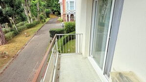 Uma varanda com vista para uma estrada e vegetação, um edifício com janelas amplas e um céu claro.