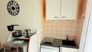 Una kitchenette compacta con cafetera, un refrigerador pequeño, microondas y un reloj en la pared.