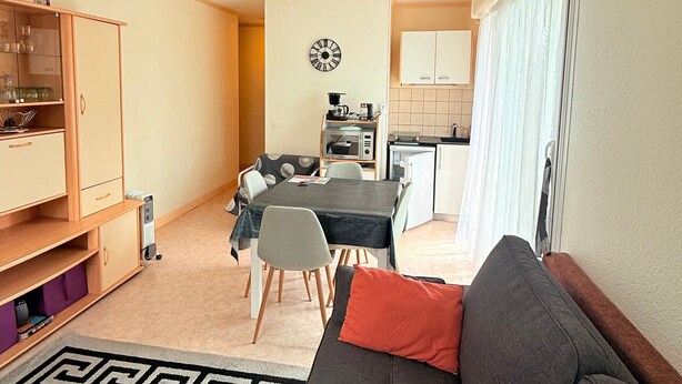 Un espacio habitable compacto con una mesa de comedor, sofá, kitchenette y un reloj en la pared.