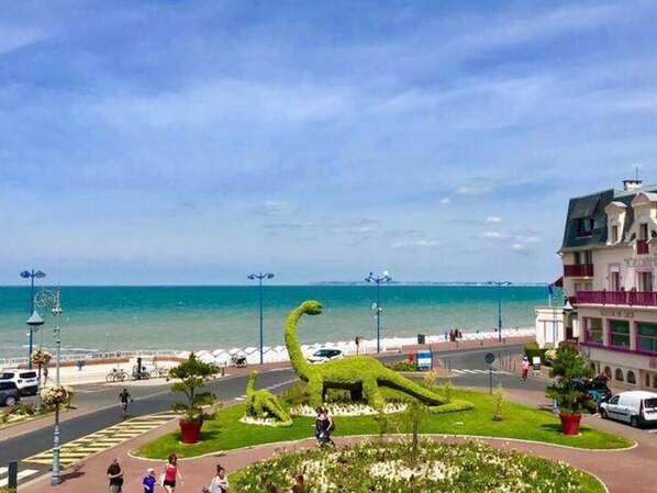 Eine Küstenlandschaft mit einem dinosaurförmigen Garten, einer Straße mit Fahrzeugen und einem Gebäude mit Balkonen.
