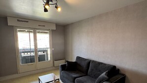 Ein modernes Wohnzimmer mit einem dunkelgrauen Sofa, zwei Holztischen und einem Schild mit der Aufschrift 'Bienvenue' über der Tür.