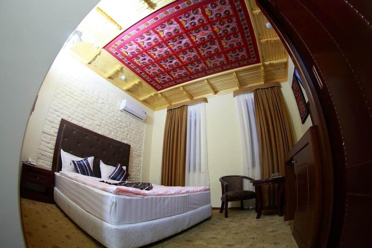 A room with a bed, a chair, a desk, and a patterned ceiling.