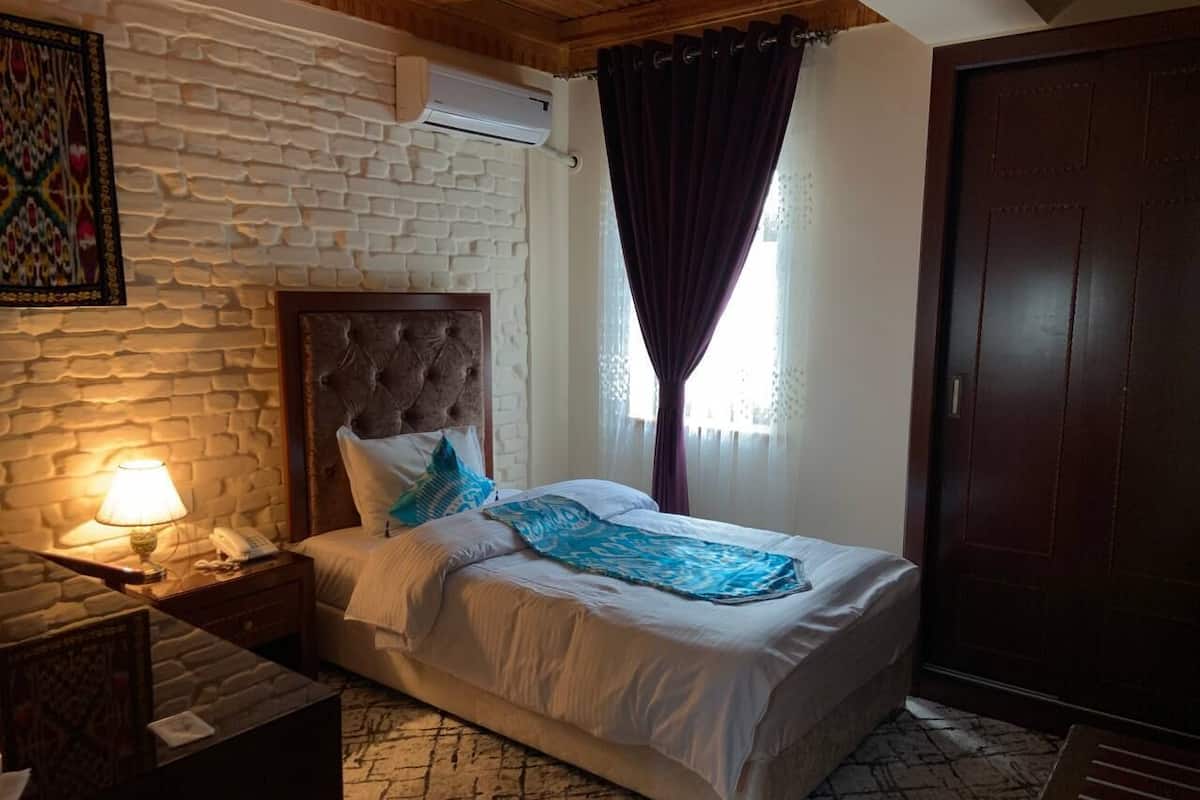 A bedroom with a stone wall, a bed with white bedding, a nightstand with a lamp, and a wooden door.
