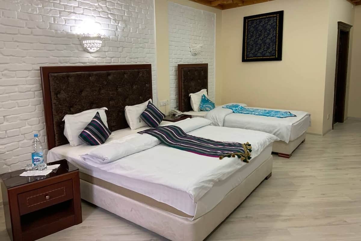 A hotel room with two beds, a brick-patterned wall, a wooden ceiling, and a framed picture on the wall.
