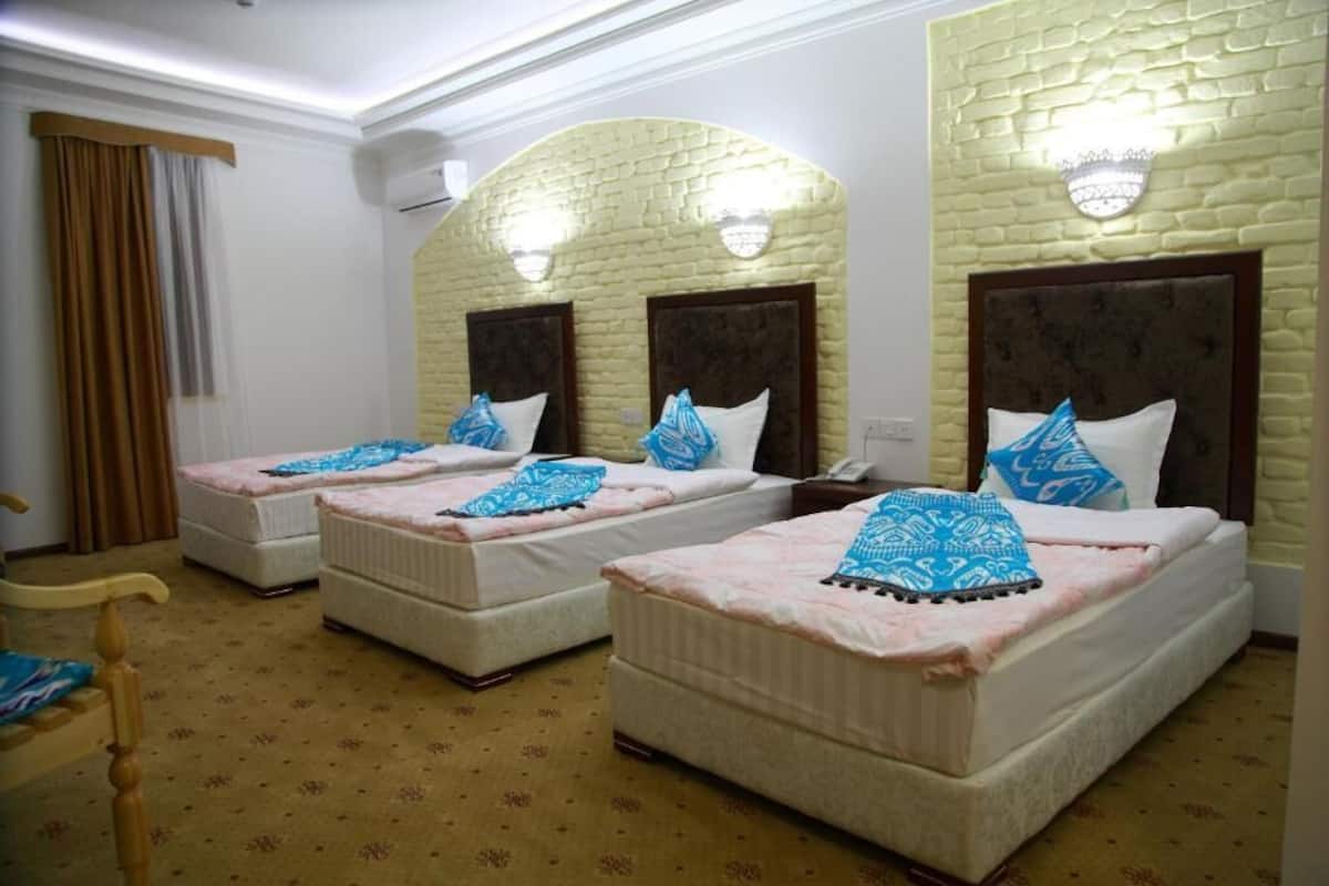 A hotel room with three single beds, each with a headboard and a decorative pillow.