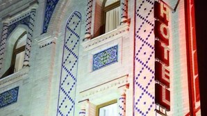 A hotel facade with intricate blue and white tile patterns, arched windows, and a prominent red neon sign. - Hotel Sultan Boutique (Samarkand)