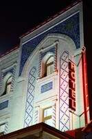 A hotel facade with intricate blue and white tile patterns, arched windows, and a prominent red neon sign.
