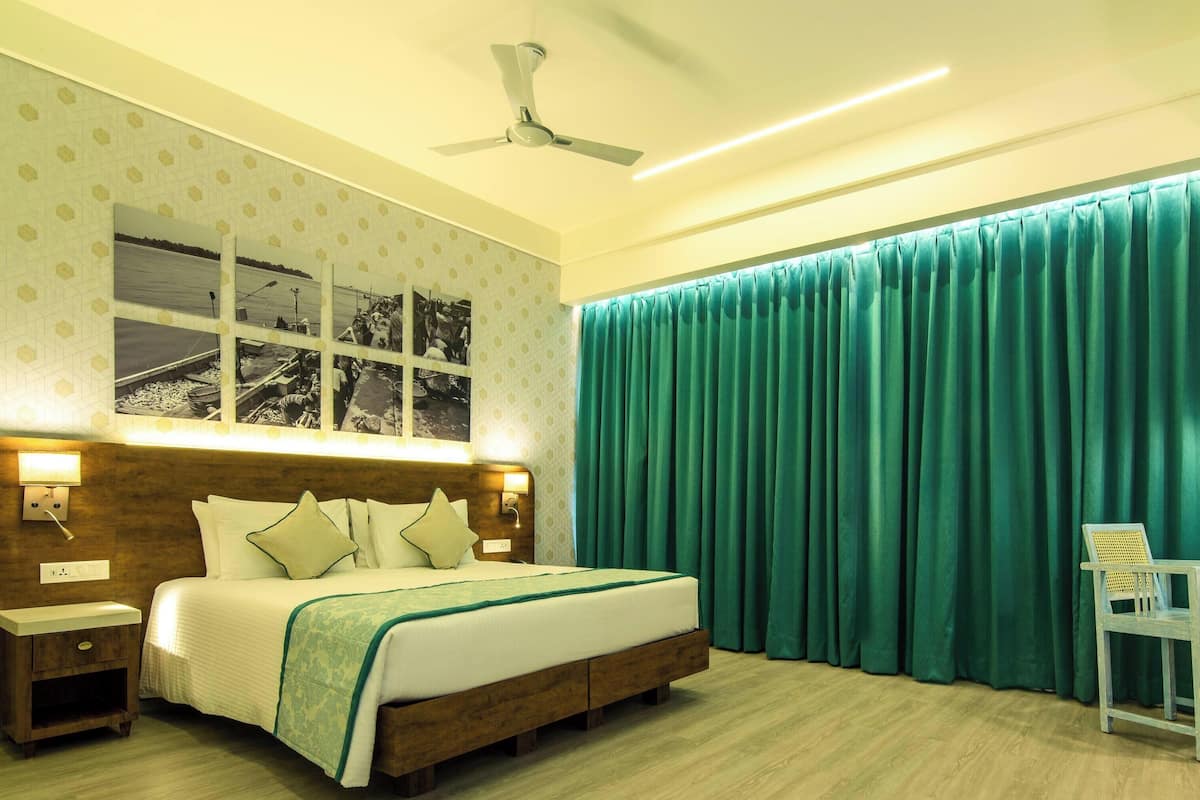 A hotel room with a bed, bedside table, nightstand, desk, chair, and a large window with curtains.