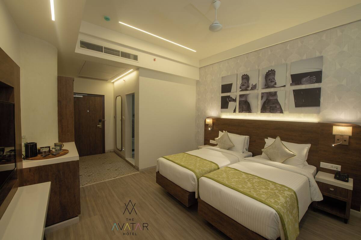 A hotel room with two beds, a desk, a mirror, and a wall with framed pictures.