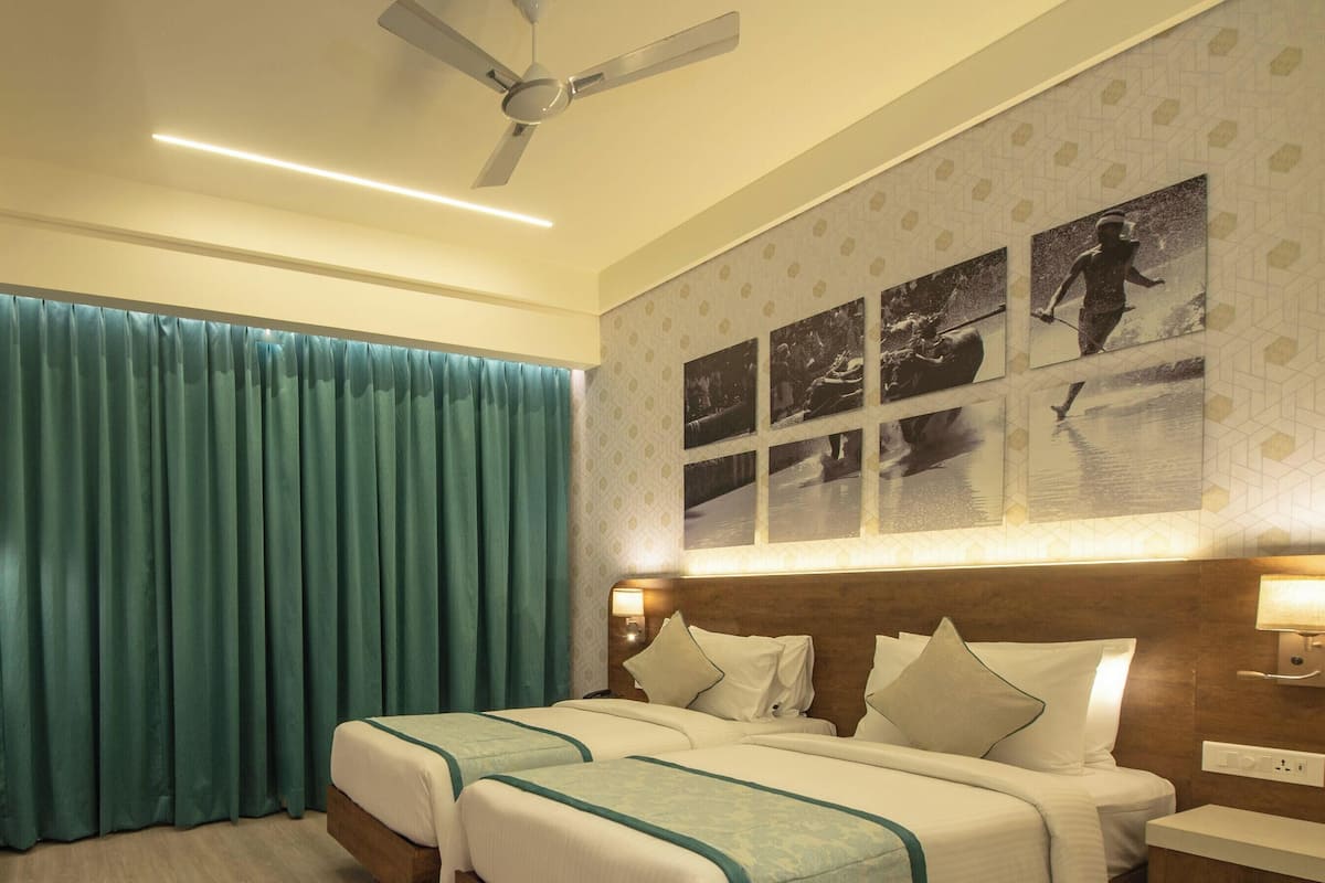 A hotel room with a bed, a TV, a ceiling fan, and a wall with framed pictures.