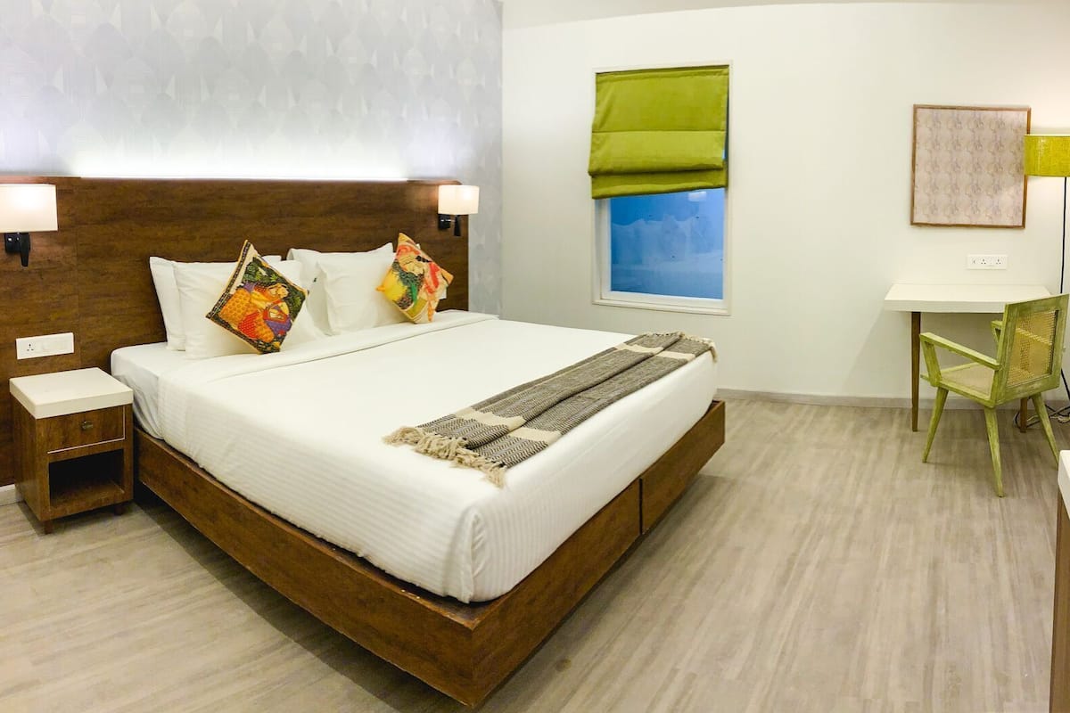A hotel room with a wooden bed, bedside tables, a desk, and a chair.