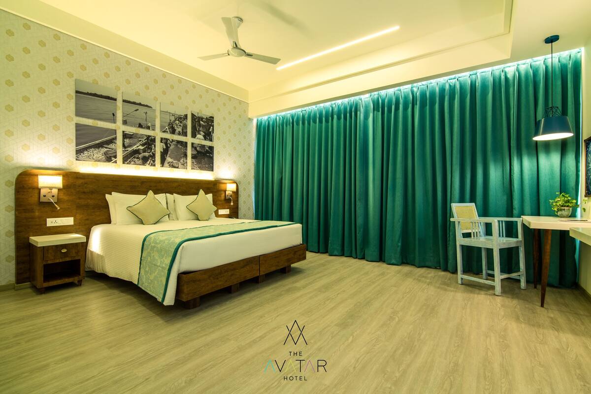 A hotel room with a bed, bedside tables, a desk with a chair, a ceiling fan, and a window with curtains.