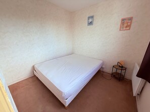 Une petite chambre avec un lit simple, un mur uni, une petite table avec une chaise et une prise de courant.