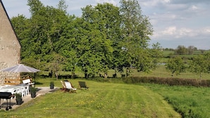 A rustic outdoor setting with a stone building, a barbecue setup, and a grassy area with trees in the background.