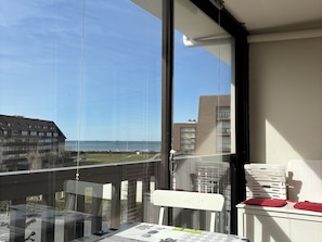 A balcony with a view of the sea, a table with newspapers, and a stack of white plastic chairs.