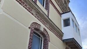 Een gebouw met een witte gevel, rode baksteen accenten rondom de ramen, en een klein balkon.