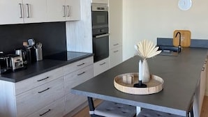 Een moderne keuken met witte kasten, een zwart aanrecht en een ronde houten tafel met een vaas.