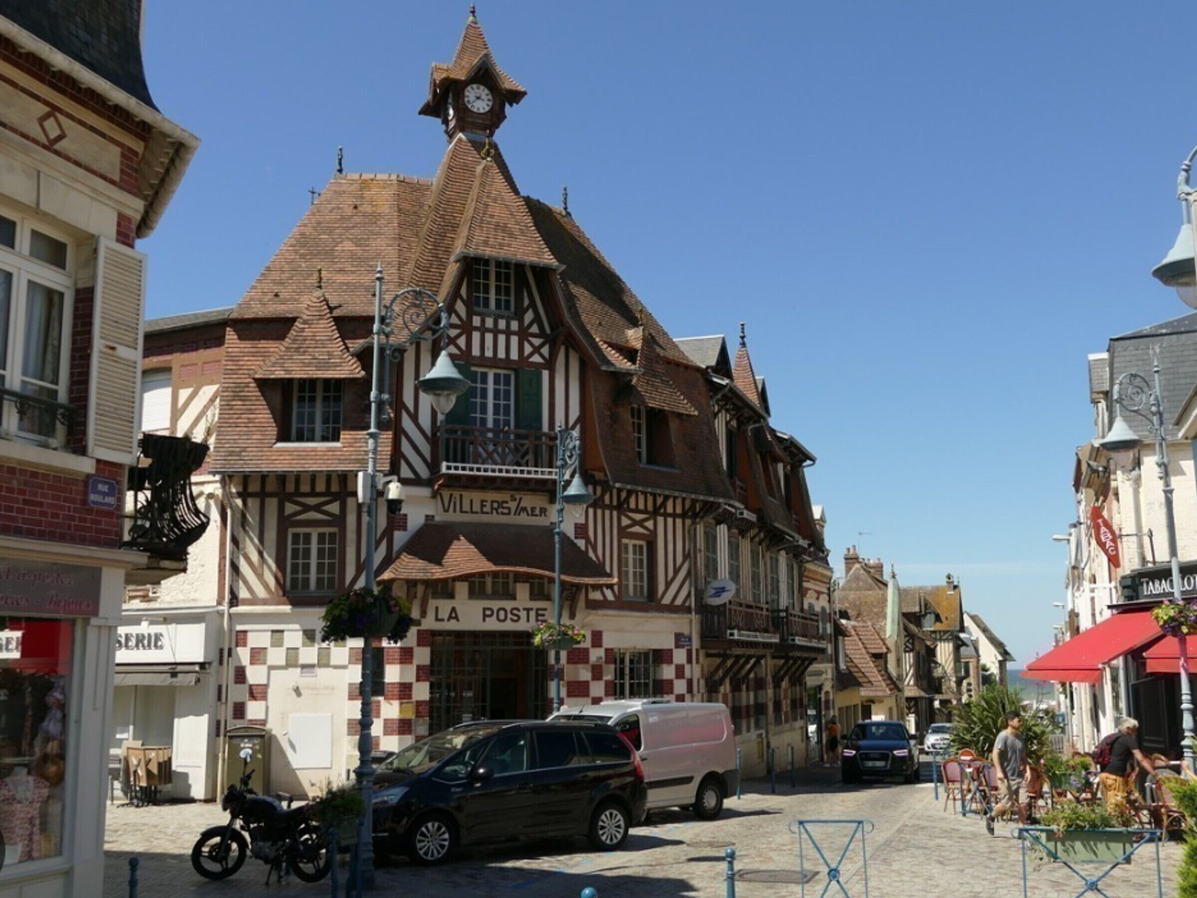 A traditional half-timbered building with a clock tower, a visible 'La Poste' sign, and a cobblestone street.