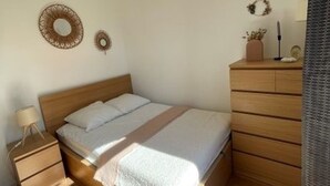 Een slaapkamer met een houten bed, een nachtkastje, een dressoir en twee decoraties aan de muur.