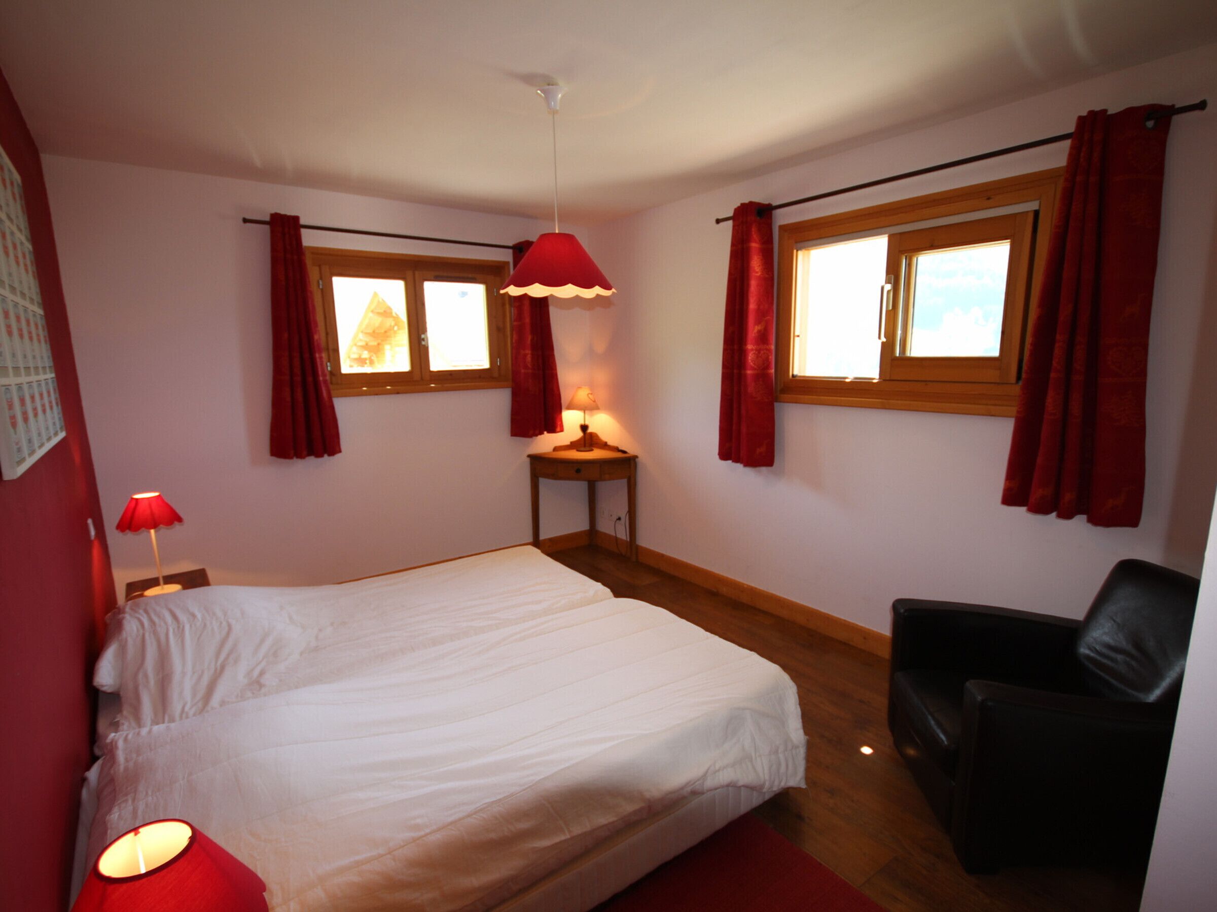 Un dormitorio con cama, escritorio, silla y dos ventanas con cortinas.