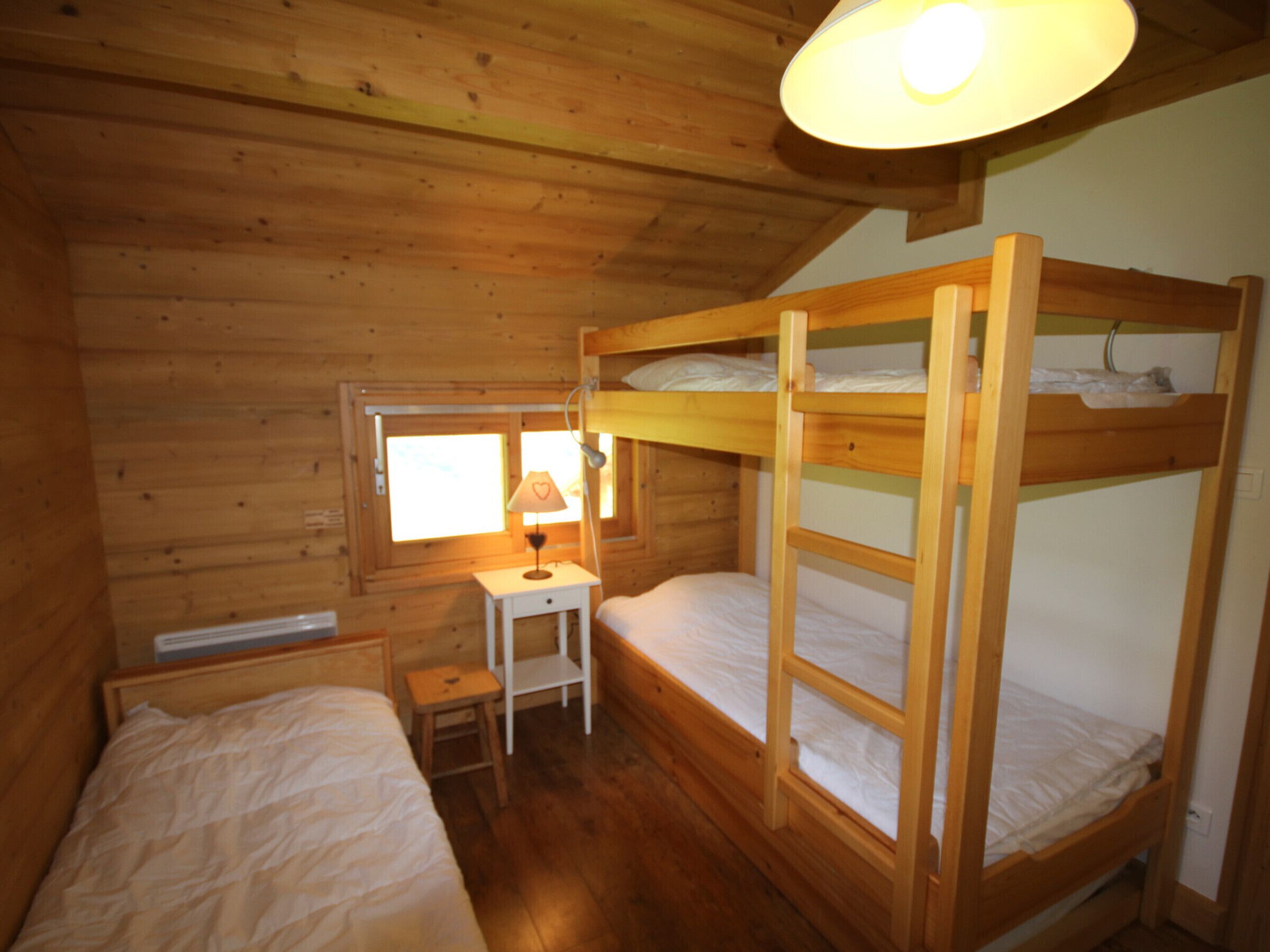 A wooden cabin bedroom with bunk beds, a small bedside table, and a window.