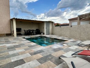 Piscina com deck revestido, área de churrasco e assentos externos.