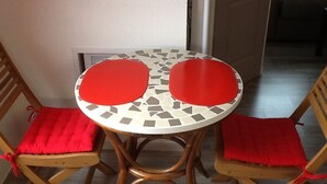 Une petite table ronde avec un plateau recouvert de mosaïques et deux chaises en bois dotées de coussins rouges.