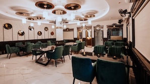 Un comedor espacioso con mesas redondas y sillas tapizadas en verde, con un diseño de techo moderno que incluye lámparas circulares.