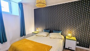 A modern bedroom with a large bed, two bedside tables with lamps, a window with curtains, and a wall with a starry pattern. - Historic 2BR Cottage with Modern Amenities & Shared Pond in Brenne Park (Communauté de communes Brenne - Val de Creuse-Douadic)