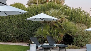 Ein Poolbereich mit Liegestühlen, Sonnenschirmen und einer gepflegten Hecke.