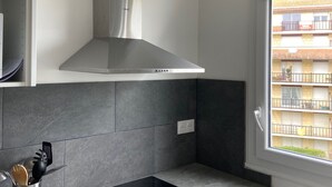 A modern kitchen with a stainless steel range hood, grey tiled backsplash, and a window with a view of a residential building. - 2-room apartment with balcony steps from the beach, WIFI and parking (Villers-sur-Mer)