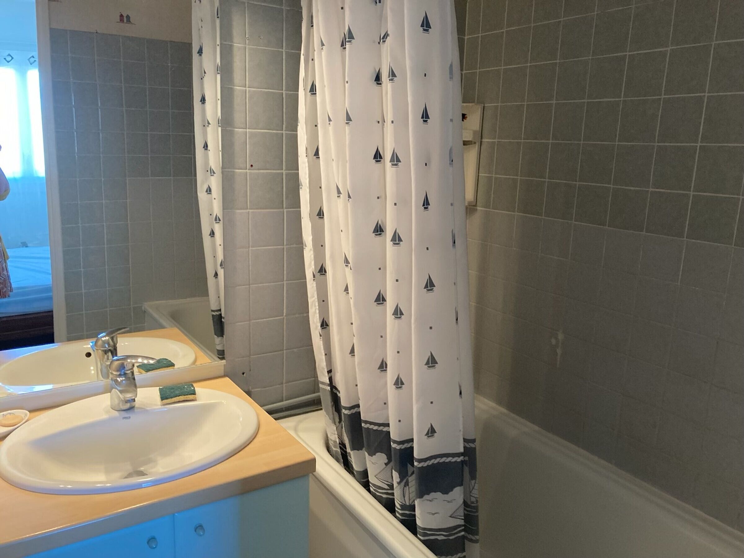 Un baño con dos lavamanos, un espejo y una cortina de ducha con estampado de velero.