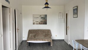 A room with a sofa, a table, and a ceiling light fixture. - 2-room apartment with balcony steps from the beach, WIFI and parking (Villers-sur-Mer)