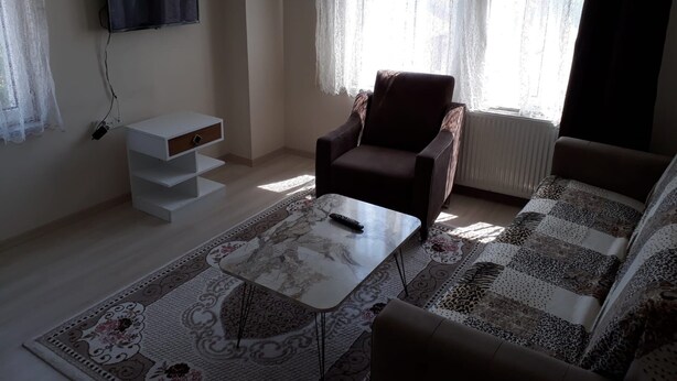A living room with a sofa, armchair, coffee table, TV, and a white storage unit. - Taner Pansiyon (Edirne)